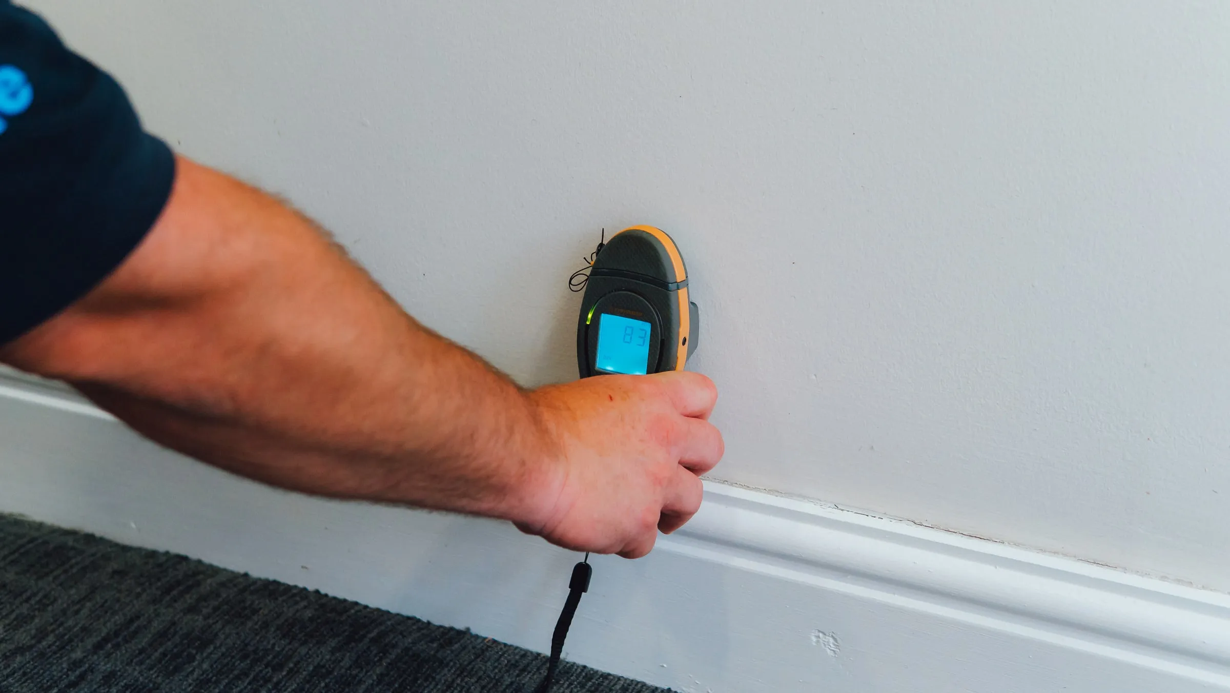 Engineer holding a moisture meter against a wall just above the skirting board