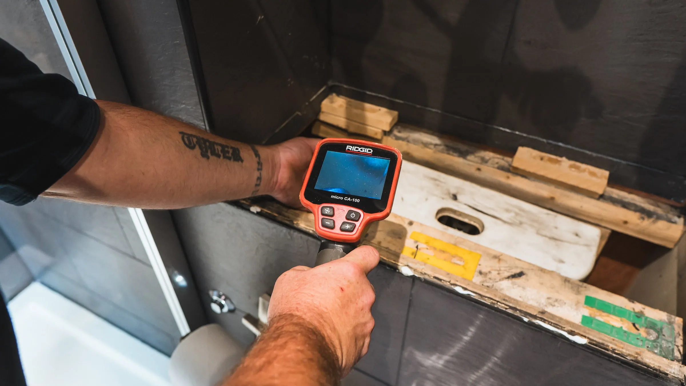 Engineer using a handheld inspection camera to look into a floor void beside a shower