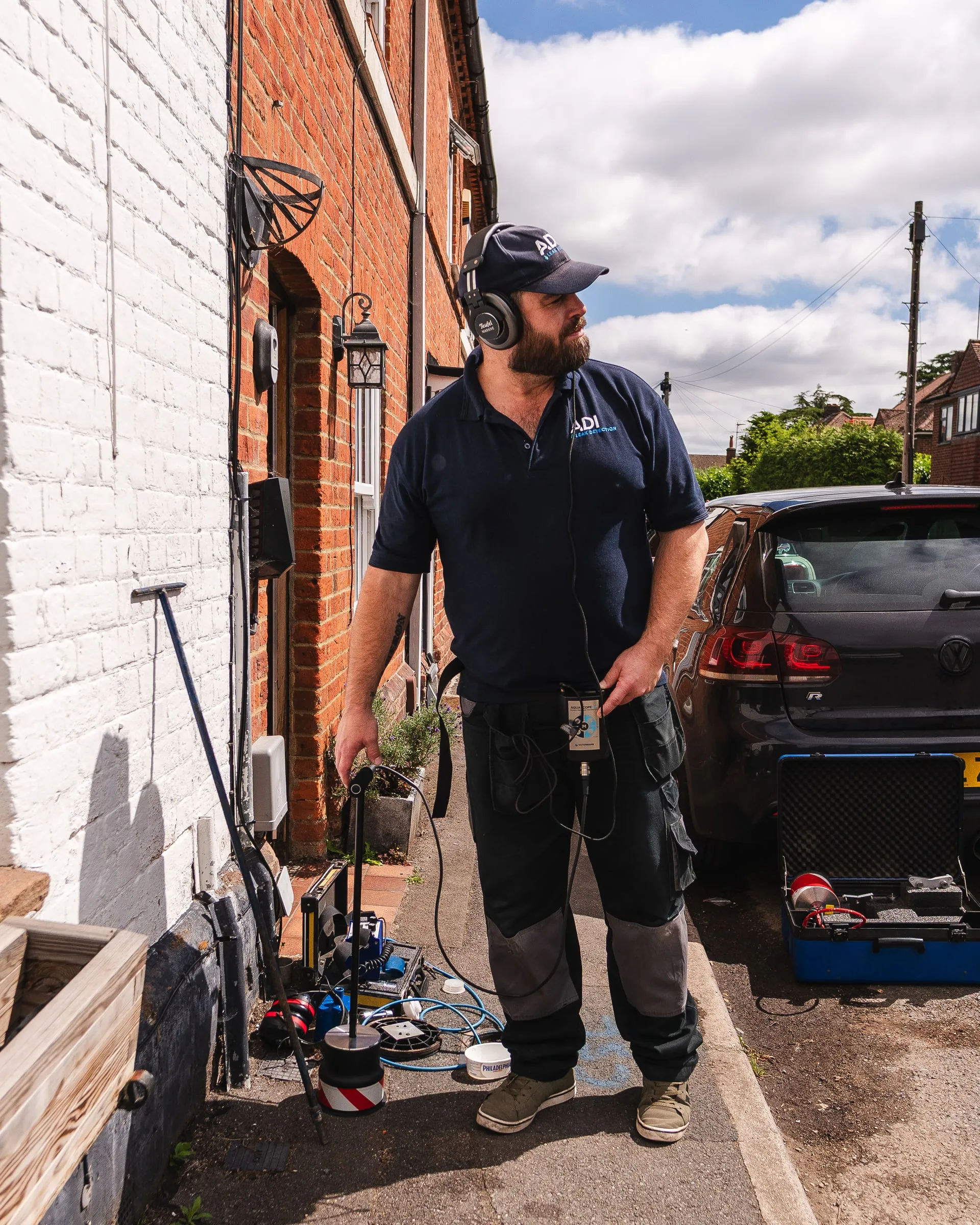 ADI engineer wearing headphones and holding an acoustic listening probe, with a ground microphone and equipment case beside him