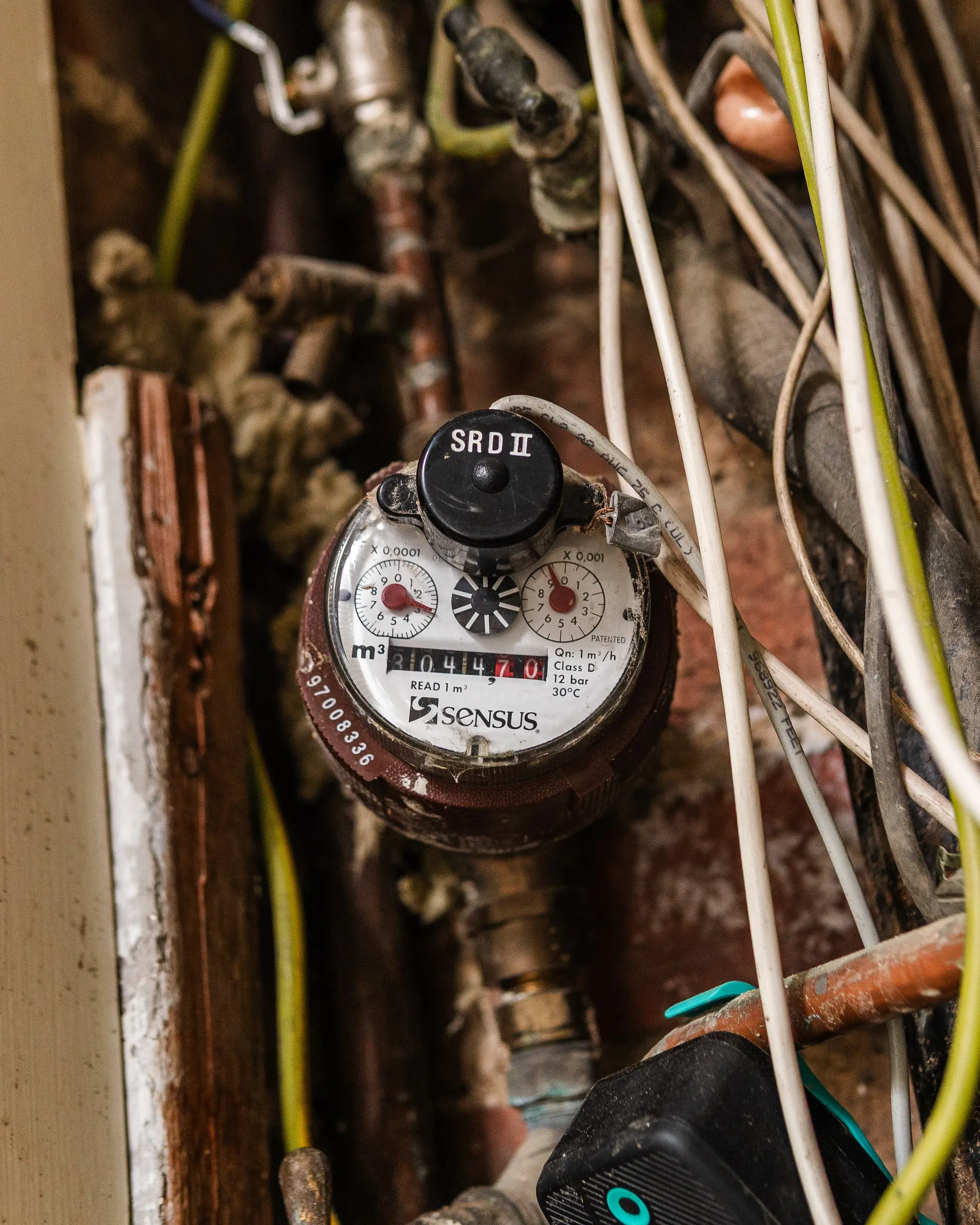 Close-up of a water meter dial in its chamber, with pipework around it