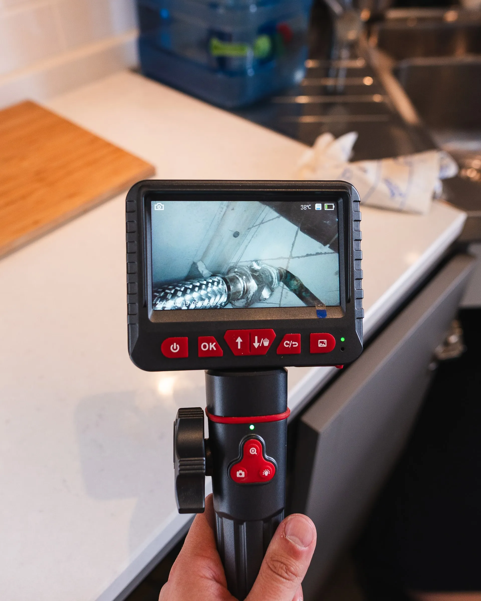 Handheld inspection camera monitor showing pipework inside a void